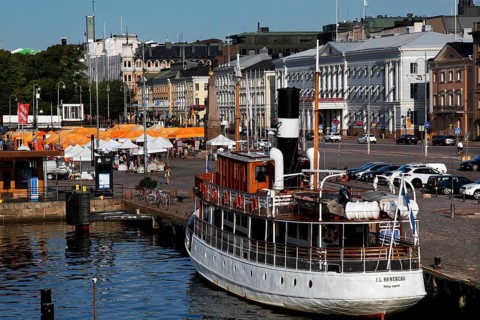 The market square in Helsinki with a boat and historic buildings along the busy harbor promenade,