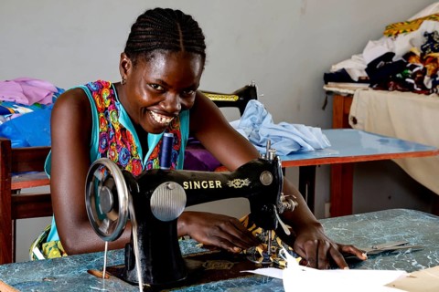 Woman working smiling on a sewing machine in a colorful sewing room, Bouaké, null, Côte d'Ivoire