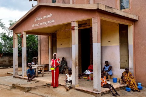 People sit and stand in front of a hospital building. The surrounding area seems quiet, Bouké,