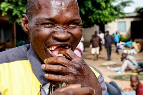 Laughing patient bites into food surrounded by other patients, Bouaké, Nimbo, Côte d'Ivoire