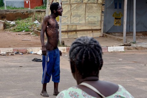 Mentally ill homeless person stands in the street while a woman sits nearby, Bouaké, Côte d'Ivoire