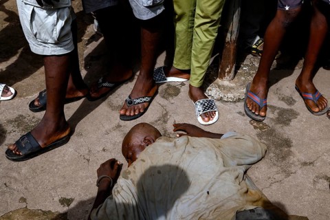 A homeless man lies asleep in the street surrounded by people, CI Bouaké, Ivory Coast