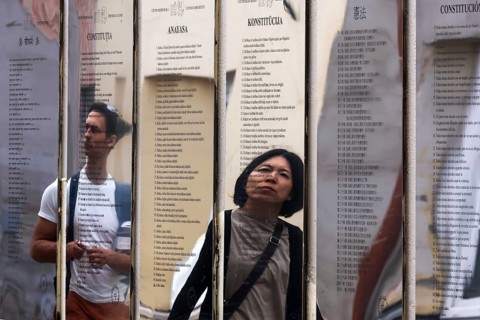 Passers-by look at the mirror installation with the Constitution of the Republic of Uzupis,