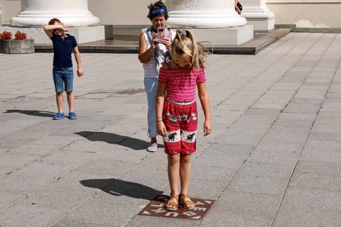 Child standing on miracle tile while tourists capture the moment, Vilnius, Vilnius County,