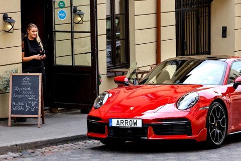 Woman standing next to a red car in front of a cafe in Uzupis, Vilnius, Vilnius County, Lithuania