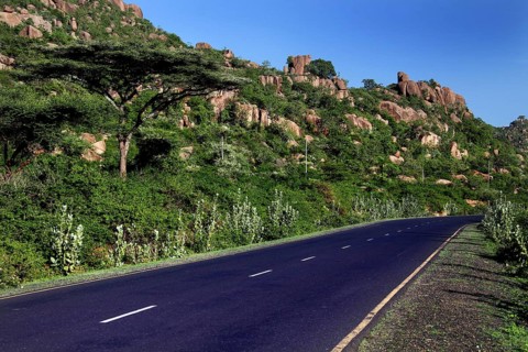 An empty road crosses a lush landscape in the Valley of Wonders under clear skies, Babile, Oromia,