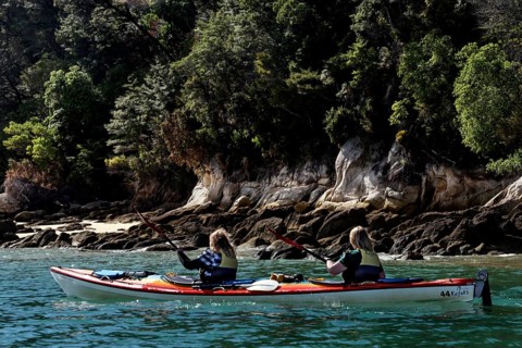 Two people paddle in a kayak along the coast of Adele Island, zero
