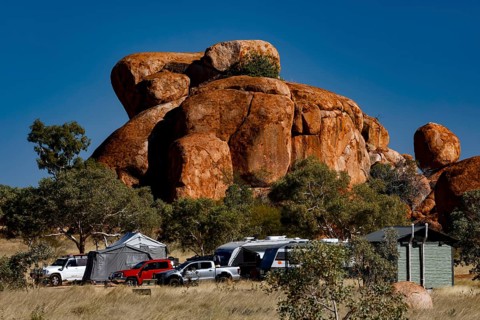 Campground surrounded by distinctive red rocks and vehicles under blue skies, Devil's Marbles,