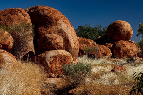 Diverse red rock formations in a sunny desert environment with natural vegetation, Devil's Marbles,