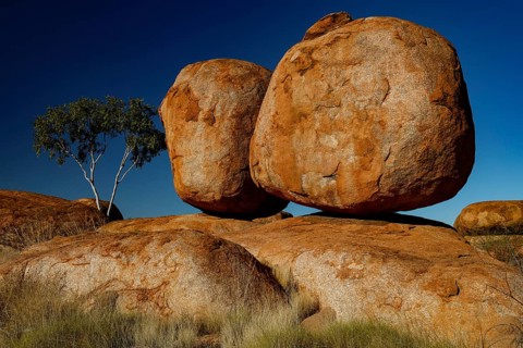 Two big rocks on top of each other, lonely tree next to it, blue sky, quiet atmosphere, zero