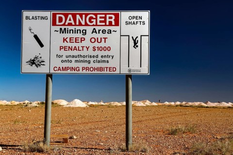 Warning sign of an opal mine in Coober Pedy with safety instructions in an arid desert landscape,