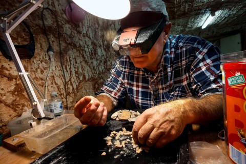 Miner examining opals at work light at Tom's Working Opal Mine, Coober Pedy, South Australia,