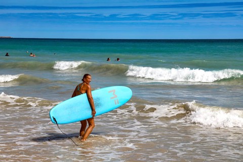 Surfer with blue surfboard standing on the water of Cable Beach, Broome, Western Australia,