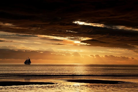 Spectacular sunset with sailboat on horizon over Cable Beach, Broome, Western Australia, Australia