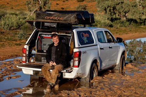 Man sits relaxed in the open trunk of a muddy off-road car on the Old Andado Track