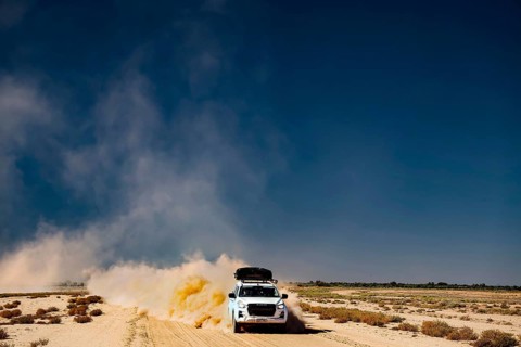 Four-wheel drive vehicle whirls up dust on desert road