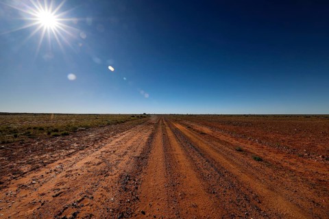 Dusty desert trail under bright sun and clear sky, Old Andado Track, Northern Territory, Australia