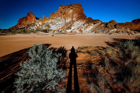 Shade stretches across the desert landscape of Rainbow Valley with distinctive rock formation, zero