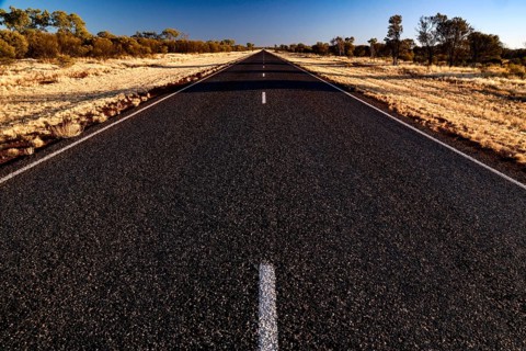 Lonely and straight desert road under clear blue sky with sparse vegetation, Stuart Hwy, Northern