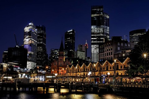 Night view of The Rocks in Sydney with illuminated former warehouses and modern skyscrapers,