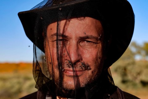 Man with a fly net over his face in front of a clear sky