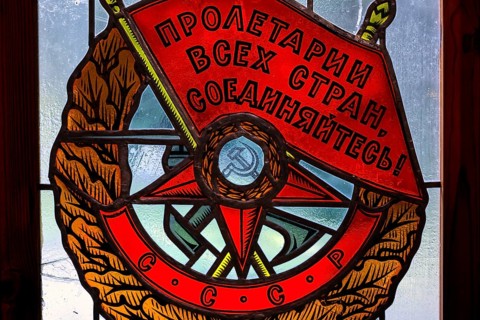 Socialist coat of arms with red banners and symbols in a stained glass window in Grutas Park,
