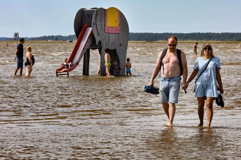 Couple walking in shallow water on a beach near an elephant water slide, Pärnu, null, Estonia