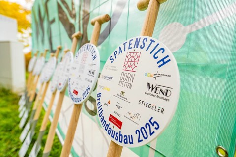 Several signs printed with logos announcing broadband expansion in 2025, fiberglass groundbreaking,