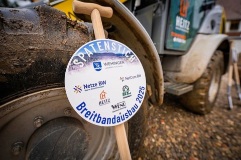A sign announces broadband expansion, in the background a wheel loader on muddy ground, fiberglass