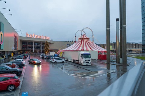 Shopping center parking lot in case of rain with illuminated circus tent at dusk, Böblingen,