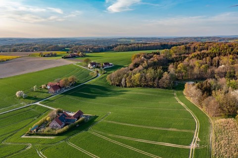 Green fields and forests with small farms under blue spring sky, oblique aerial view, Osnabrücker