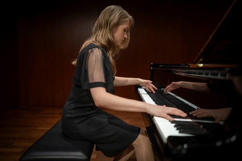 Young woman, pianist, side view playing on a Steinway & Sons grand piano in evening dress,