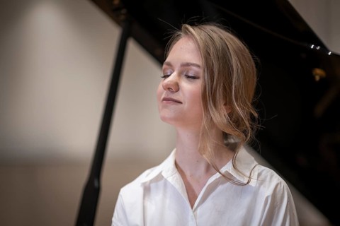 Dreamy looking young woman, pianist, wearing white blouse in front of Steinway & Sons grand piano,