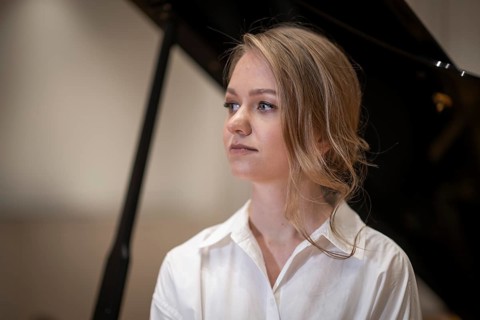 Serious looking young woman, pianist, wearing white blouse in front of Steinway & Sons grand piano,