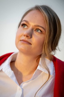 Portrait of a thought-looking young woman, pianist, wearing white blouse and red cardigan, in the