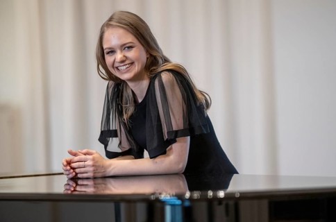 Laughing young woman, pianist, in evening dress leaning on a Steinway & Sons grand piano,