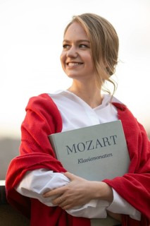 Smiling young woman, pianist, in white blouse and red cardigan, in the evening light, holding notes