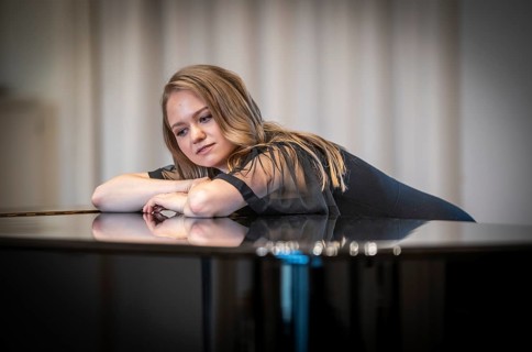 Thought-looking young woman, pianist, in evening dress leaning on a Steinway & Sons grand piano,