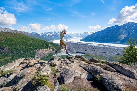 Young man jumping into the air, view of impressive mountain landscape with Matanuska glacier and