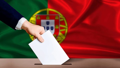 Hand placing a ballot in ballot box with the Portuguese flag in the background. Portugal