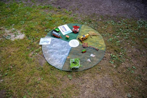 Circular outdoor table with toy vehicles on a grassy area, playful presentation of the individual