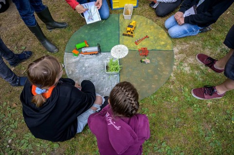 Children look at an agricultural model on the ground in a garden area, event for schoolchildren of