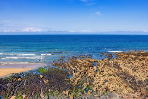 Rocky seashore in low tide with rolling sea waves and a seascape view to the horizon on a sunny