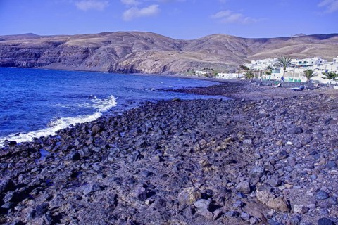 Rocky coastal landscape with blue waves and a village at the foot of the mountains under clear