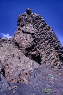 View of a high volcanic rock structure under a clear blue sky, partial view of El Cuervo volcano,