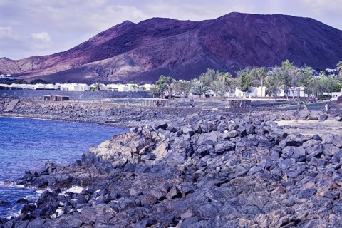 Rugged coastal area with rocks and views of reddish brown mountains under cloudy sky, Playa Blanca