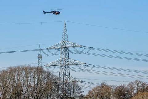 A helicopter flies over trees and power poles in a landscape during technical use, Lemförde, Lower