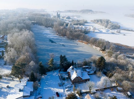 Snowy landscape with a frozen lake surrounded by trees and houses in fog, aerial view, Oelsburg,
