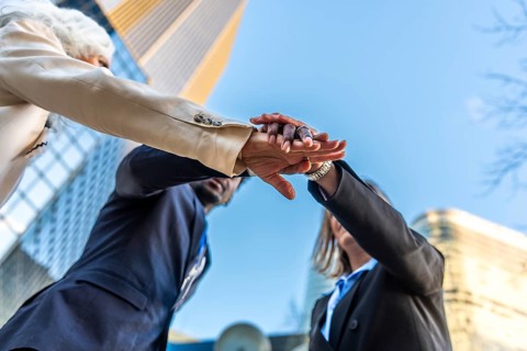 Diverse business team stacking hands outdoors in an urban setting, symbolizing unity,
