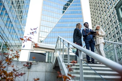 Diverse business professionals smiling and interacting while looking at a tablet on modern outdoor